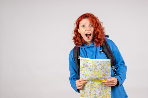情感年轻女性的正面图 白色墙上有背包和地图前方成人假期