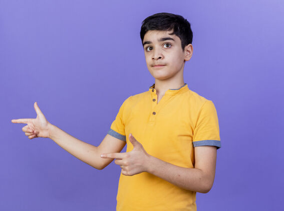 手势令人印象深刻的年轻白种人男孩指着一边孤立的紫色墙壁与复制空间指点年轻人男孩
