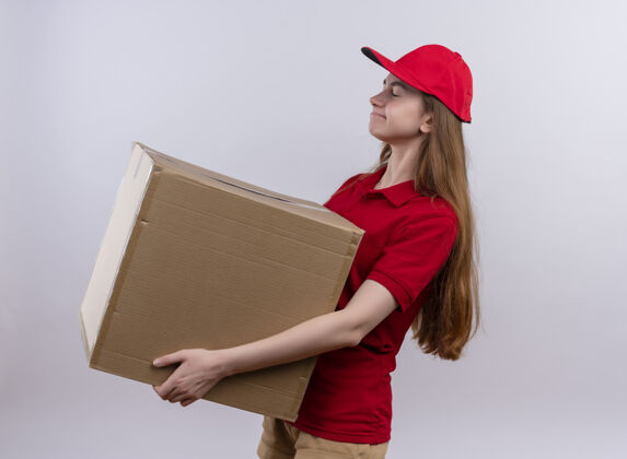 抱着疲惫的年轻送货女孩 穿着红色制服 站在隔离的白色墙壁上的侧视图中疲惫制服站着