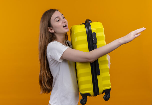 侧板年轻的旅行家女孩拿着手提箱 伸出手 看着右边的橘黄色墙壁上的复制空间手右边手提箱