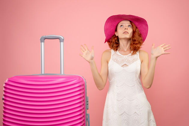 航行年轻的女性游客与粉红色的帽子和粉红色的墙壁上的包的正面视图旅行夏天可爱