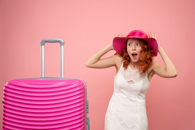 夏天年轻的女性游客与粉红色的帽子和粉红色的墙壁上的包的正面视图可爱包航行