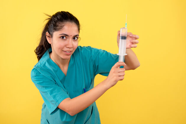 年轻女医生年轻女医生在黄色墙上展示注射器的正视图工作注射器正面