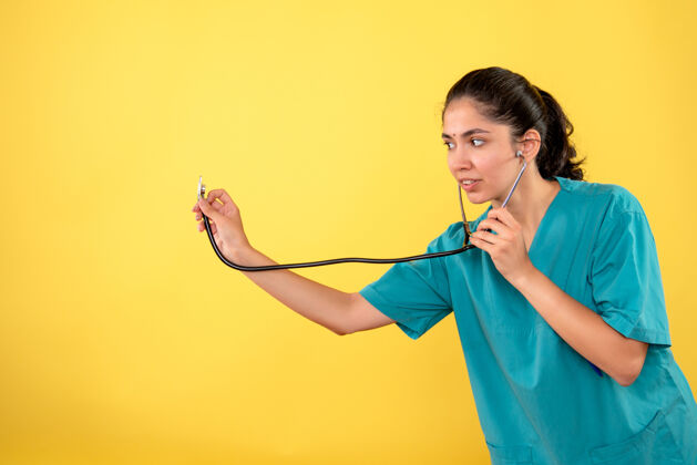 成人黄色墙上手持听诊器的年轻女医生的正视图前面人女士