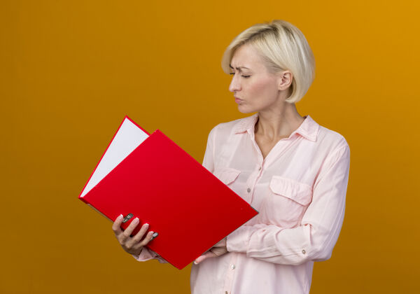 年轻想着年轻的金发斯拉夫女人抱着文件夹看着孤立在橙色墙上文件夹思考抱着