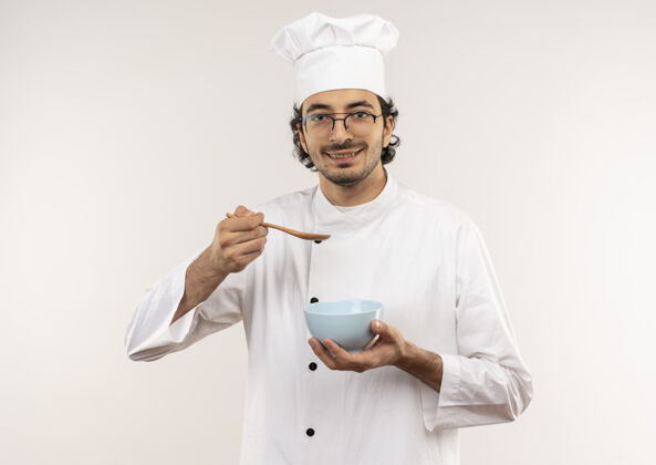 拿着年轻的男厨师穿着厨师制服 戴着眼镜 拿着勺子 碗被隔离在白色的墙上厨师碗穿