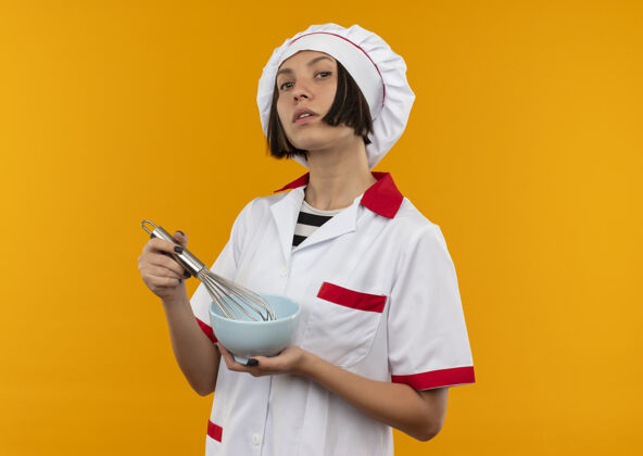 空间自信的年轻女厨师 身着厨师制服 手拿搅拌器和碗 在橘子上隔离 留有复制空间橙色制服厨师