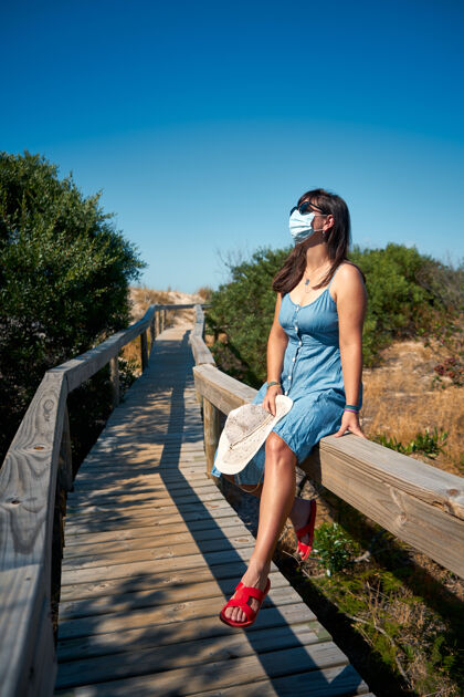 夏季戴着一次性口罩的女游客坐在桥上女性休闲安全