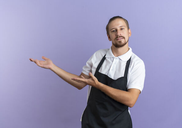 手自信的年轻帅哥理发师穿着制服 用手指着一边孤立的紫色自信帅气理发师