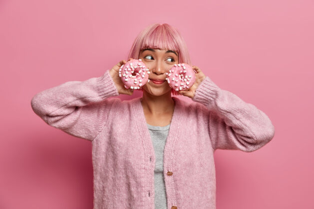 风格快乐的女人 粉色的发型 拿着两个油炸圈饼 摆姿势卡路里亚洲少女