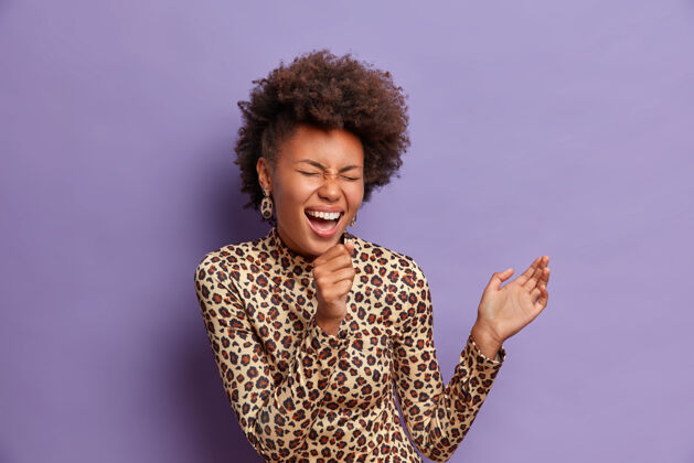 高领毛衣快乐的非洲裔美国妇女的照片 手握在嘴边作为麦克风 在卡拉OK里唱歌 心情愉快 穿着豹纹衣服豹纹乐趣欢乐