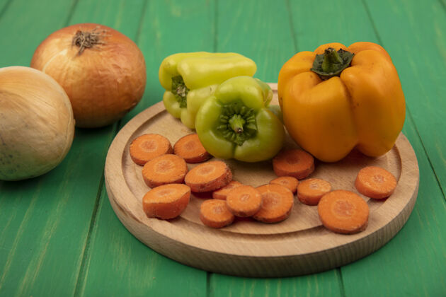 胡椒顶视图黄色和绿色的甜椒在一个木制的厨房板与切碎的胡萝卜和洋葱隔离在绿色的木墙上自然观点顶部