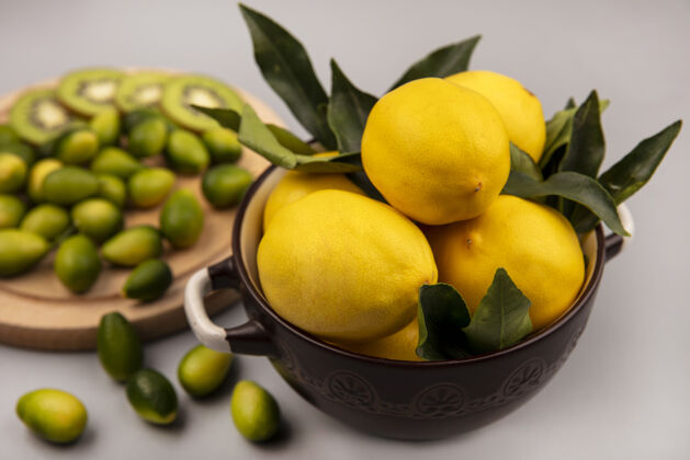 板白色墙壁上的木制厨房板上 碗里放着新鲜的黄色柠檬 还有金盏花和猕猴桃片顶部柑橘配料