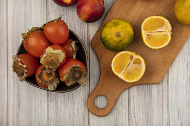 碗健康的橘子放在木制的厨房板上 柿子放在碗里 桃子被隔离在灰色的木墙上桃子新鲜厨房