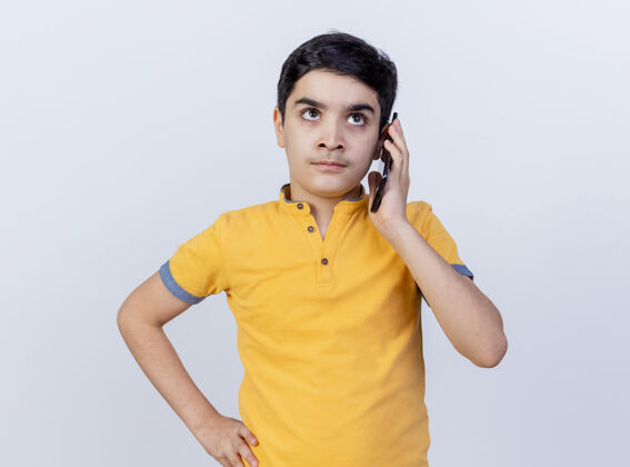 腰部皱眉的年轻白人男孩在讲电话 手放在腰上 在白色背景下孤立地抬头看手电话男孩