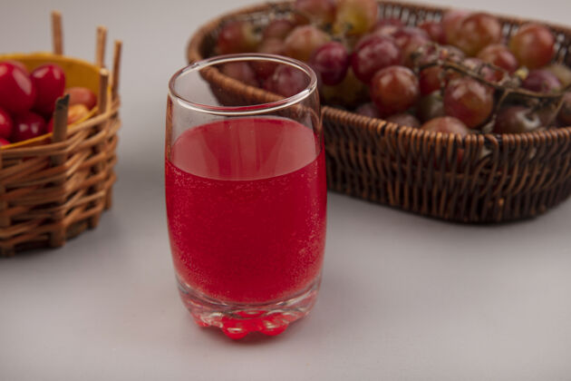 玻璃杯在灰色的墙上 一个桶上放着葡萄 杯子里放着新鲜的山茱萸樱桃汁新鲜视野葡萄