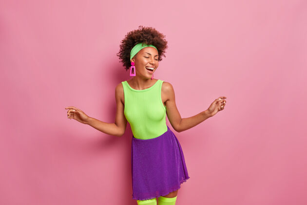 年轻乐观的女人喜出望外 做些动作 举手 跳胜利舞 穿绿紫色的衣服 闭上眼睛积极有趣微笑