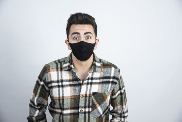 男性戴着黑色防冠状病毒面具的年轻人站在白墙上的照片安全病毒预防