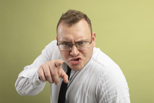 男人皱眉的成年斯拉夫男子戴着眼镜 打着领带 看着并指着橄榄绿背景上孤立的摄像机斯拉夫领带穿