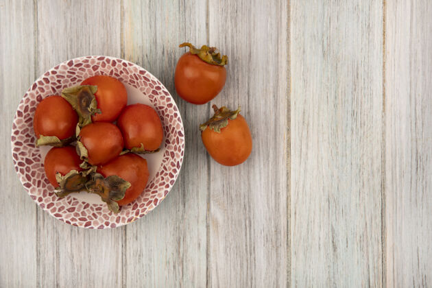 新鲜一个碗上多汁的软柿子的俯视图 柿子被隔离在灰色的木墙上 有复制空间食物多汁木头