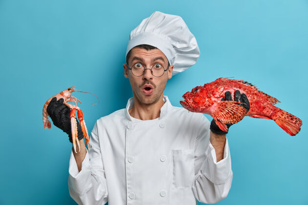 专业照片中的厨师手握小龙虾 红鲈鱼 用海鲜烹制美味佳肴 在他的鱼菜单上工作 惊奇地张大嘴巴鱼海鲜人
