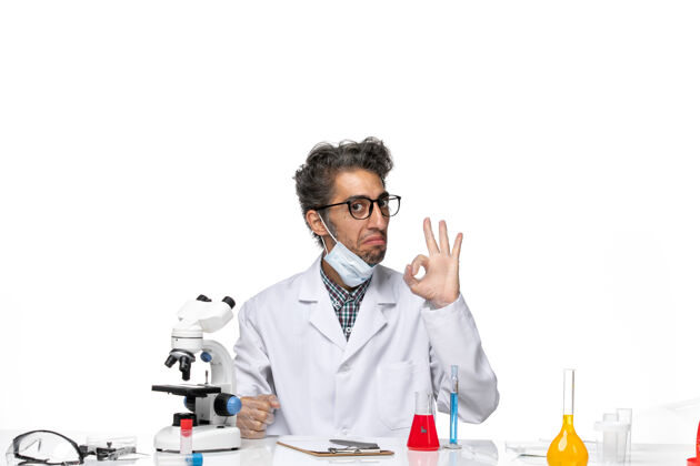 前面正面图身着特殊套装的中年科学家围坐在桌子旁 拿着解决方案专业桌子听诊器