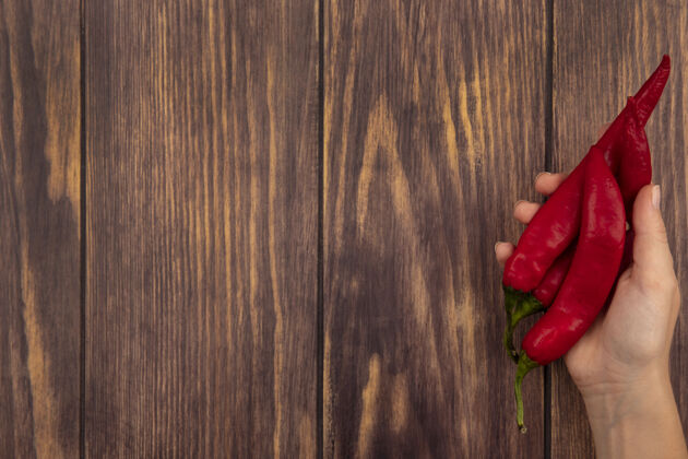 观点顶视图的女性手拿着新鲜的红辣椒在木墙上复制空间举行顶部烹饪