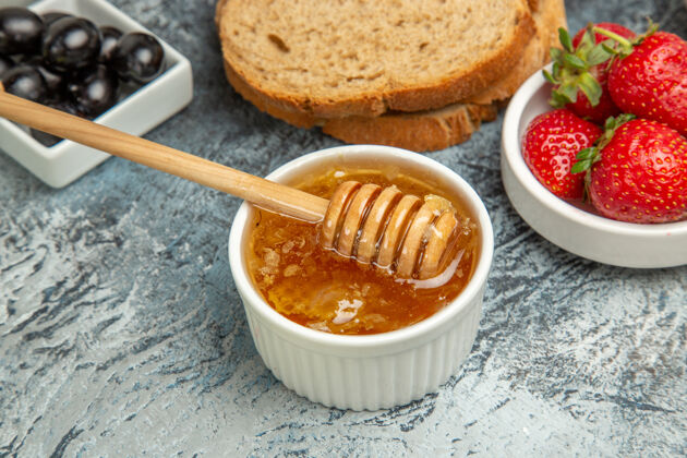 午餐正面图新鲜草莓配茶面包和蜂蜜 深色地板上水果甜食面包前面盘子
