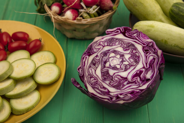 自制新鲜的紫色卷心菜 黄瓜和西葫芦放在碗里 萝卜放在桶里 切碎的西葫芦片和李子西红柿放在绿色的木墙上的盘子里西红柿李子食物