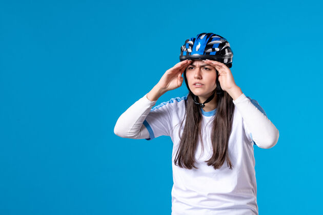 人前视图穿着运动服戴着头盔的年轻女性在蓝色的墙上遥望远方视图年轻女性头盔