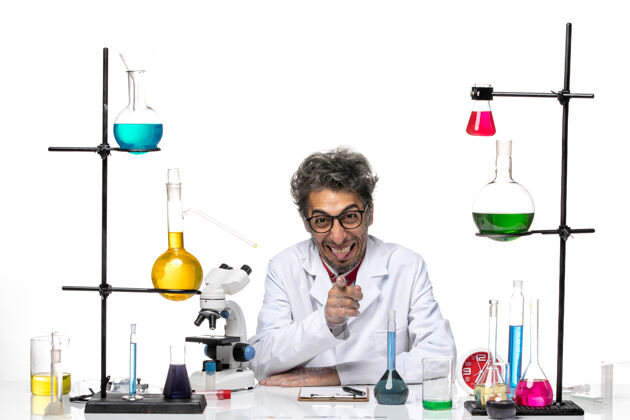医疗前视图穿着白色医疗服的男科学家坐在桌子前 带着解决方案坐着视图化学