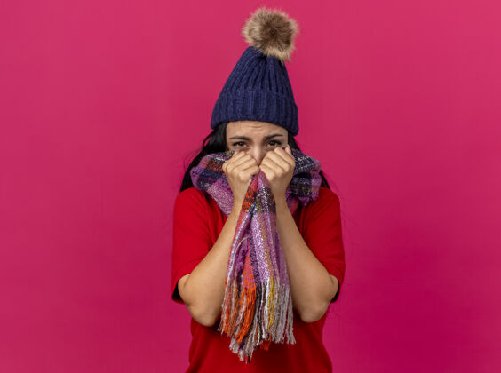 立场寒风凛冽的年轻病妇戴着冬日的帽子和围巾捂着嘴用围巾看着隔离在粉色墙上的前面脸穿着人