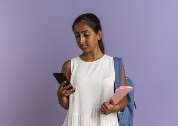 年轻年轻的女学生背着书包拿着笔记本 看着手里的手机就发紫了背笔记本手