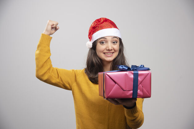 礼品盒戴着圣诞帽的黑发女人伸出拳头 手里拿着礼盒人漂亮庆祝