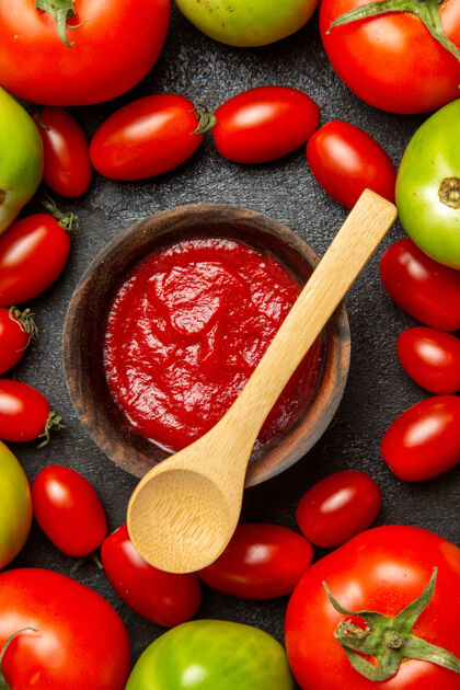李子西红柿顶部近距离观看樱桃红色和绿色的西红柿周围的碗番茄酱和一个木勺在黑暗的地面上碗西红柿食物