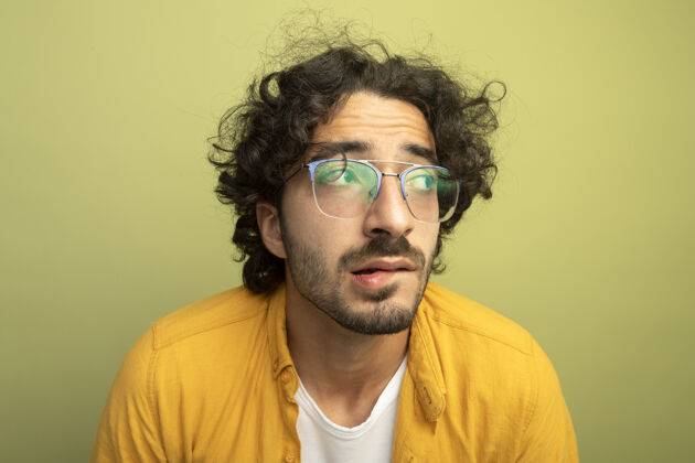 特写特写镜头：焦急的年轻帅哥戴着眼镜 看着隔离在橄榄绿墙上的咬着嘴唇人男人嘴唇