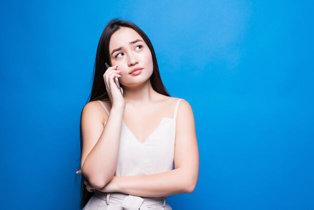 肖像年轻漂亮的亚洲女人在蓝色的墙上用手机聊天手机人休闲