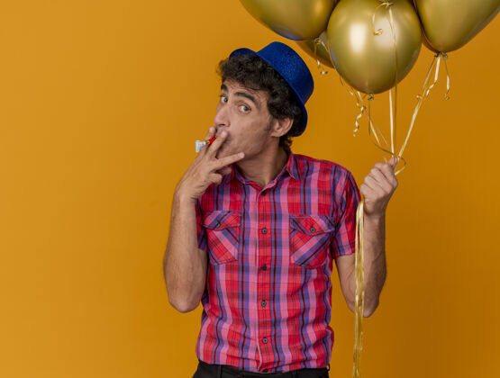 脸印象深刻的中年党人戴着党的帽子拿着气球看着前面假装吸烟用党的吹风机香烟隔离在橙色的墙上吹风机穿表情