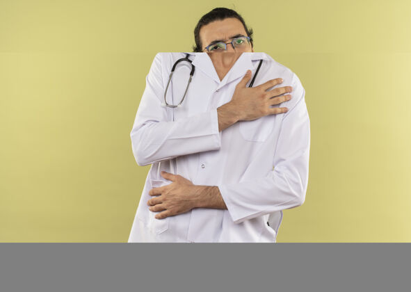 医生生病的年轻男医生戴着眼镜 穿着白色长袍 手持听诊器 手放在绿色的肩膀上绿色听诊器白色