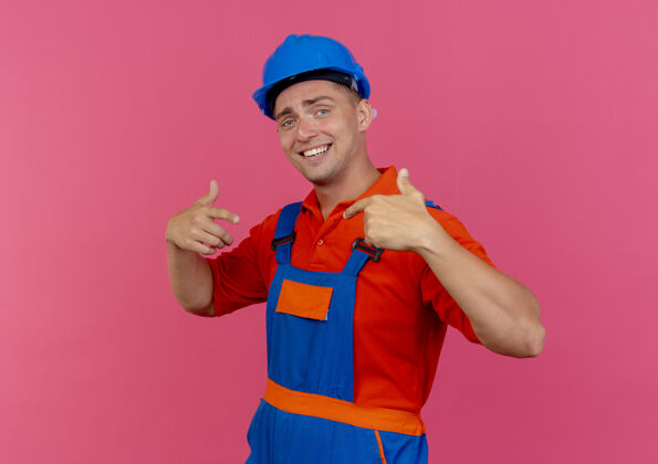 他自己身穿制服 头戴安全帽 面带微笑的年轻男性建筑工人指着自己站在粉红色的地板上安全制服建设者