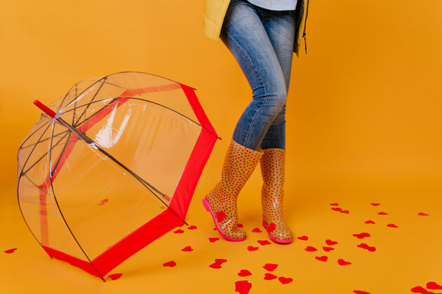 肖像穿着蓝色牛仔裤的苗条女士站在铺着纸心的地板上穿着胶鞋的女模特在红阳伞旁摆姿势天气姿势年轻