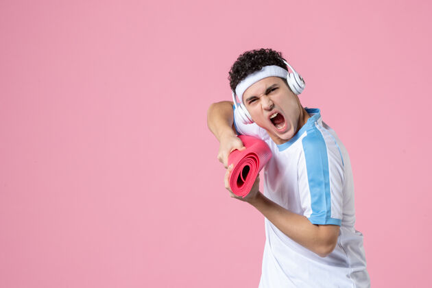 视图正面图愤怒的年轻男子穿着运动服 拿着瑜伽垫人球垫子