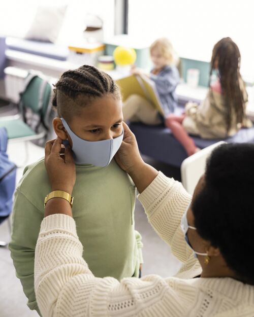 孩子老师帮助一个学生戴上医用口罩知识学习面具