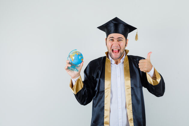 前面年轻人拿着学校的地球仪 穿着研究生制服竖起大拇指 看上去很幸运正视图欢呼自信毕业