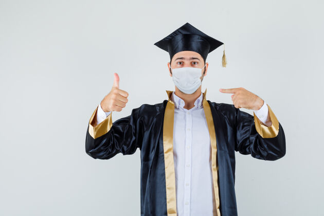面具年轻人指着自己的面具 大拇指朝上 穿着毕业制服 正面照肖像自信男