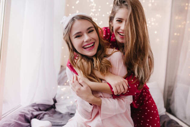 朋友早上 女孩带着真诚的微笑拥抱着朋友卧室里 长发的姐妹们拥抱在一起兴奋漂亮休闲