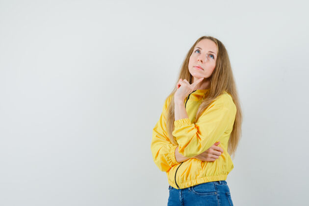 模特身穿黄色棒球服和蓝色牛仔裤的年轻女子站在思考的姿势中 神情沉思前视图休闲立场年轻