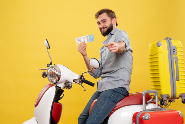 持有旅游概念与年轻的微笑胡须男子坐在摩托车上 并指出向前举行的黄色车票摩托车向前成人