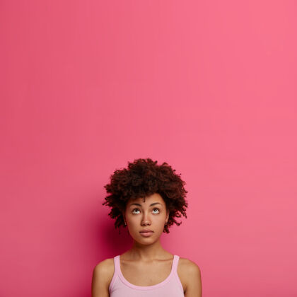 向上自然卷曲的非洲裔美国女人看上去若有所思 心中有数 穿着休闲服 站在粉色的墙上 为你的晋升复制空间 回忆一些事情思想沉思人
