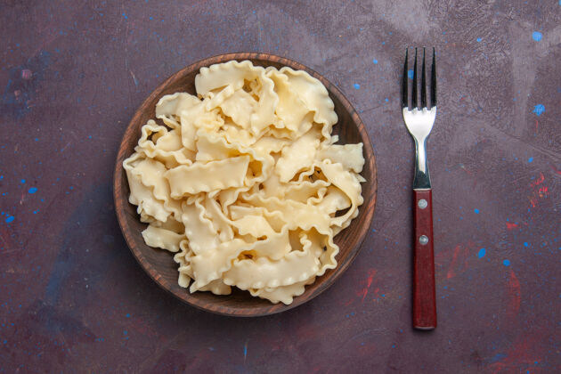 意大利面顶视图切片生面团在棕色盘子里黑暗的背景餐食品晚餐面团生的盘子抹刀